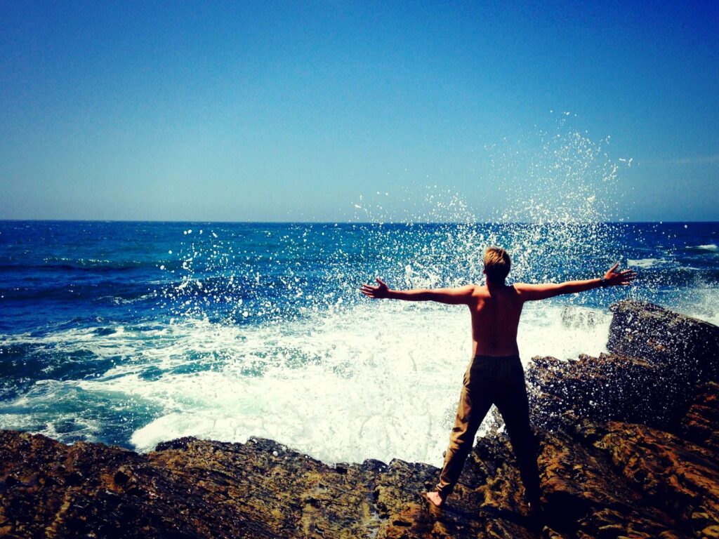 Person standing on coastal rocks with arms open toward the ocean, representing clarity, freedom, and new direction